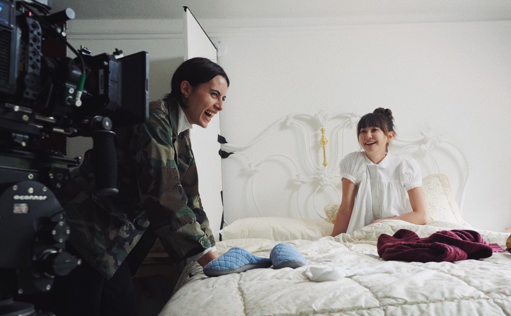 A camera in the foreground is aimed at two laughing women, a filmmaker and her actor.