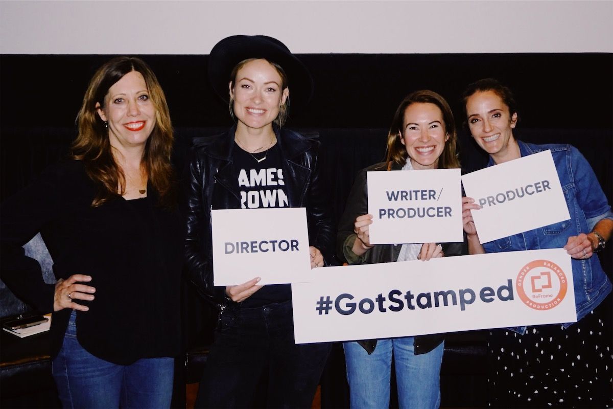 Four women smile in front of a theater screen holding signs with their crew titles on them.