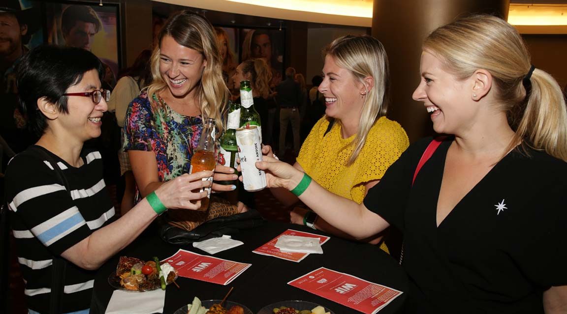 http://Four%20laughing%20women%20clink%20their%20beer%20bottles%20for%20a%20toast%20at%20a%20reception%20following%20a%20film%20screening.