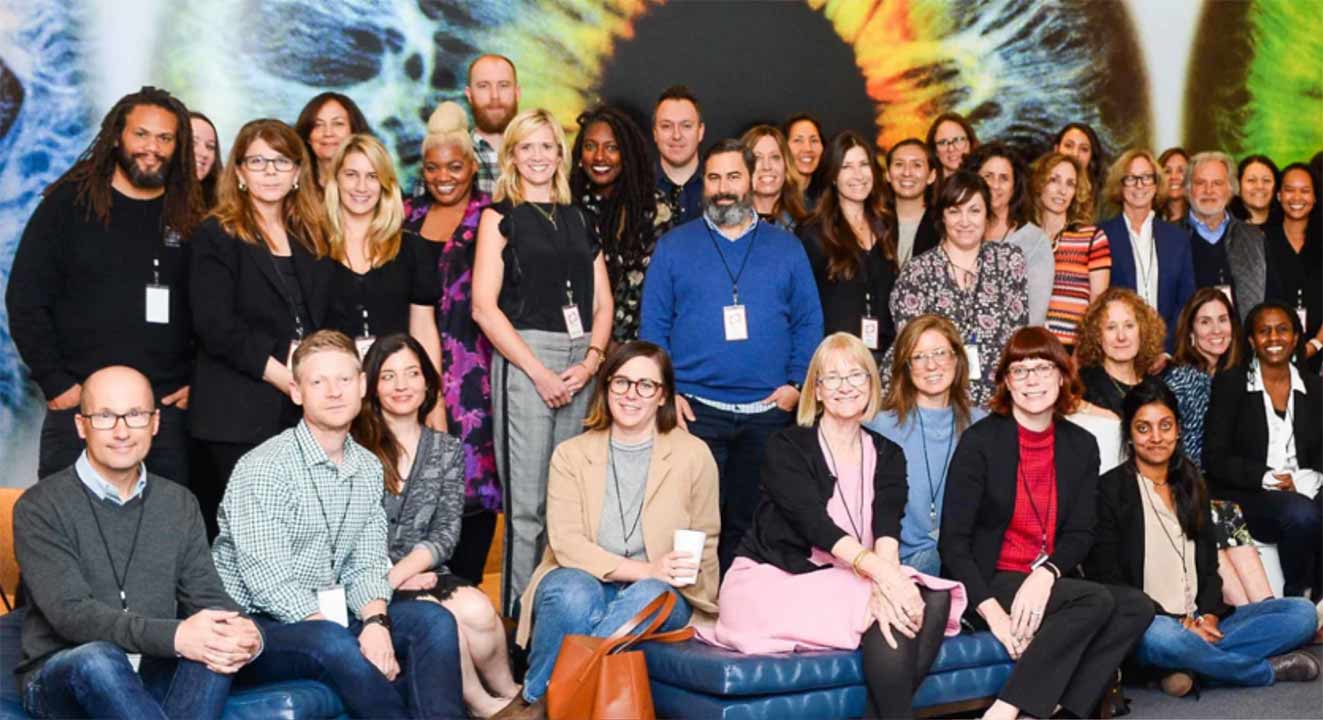 A large group of people smile for a posed photo in front of a mural.